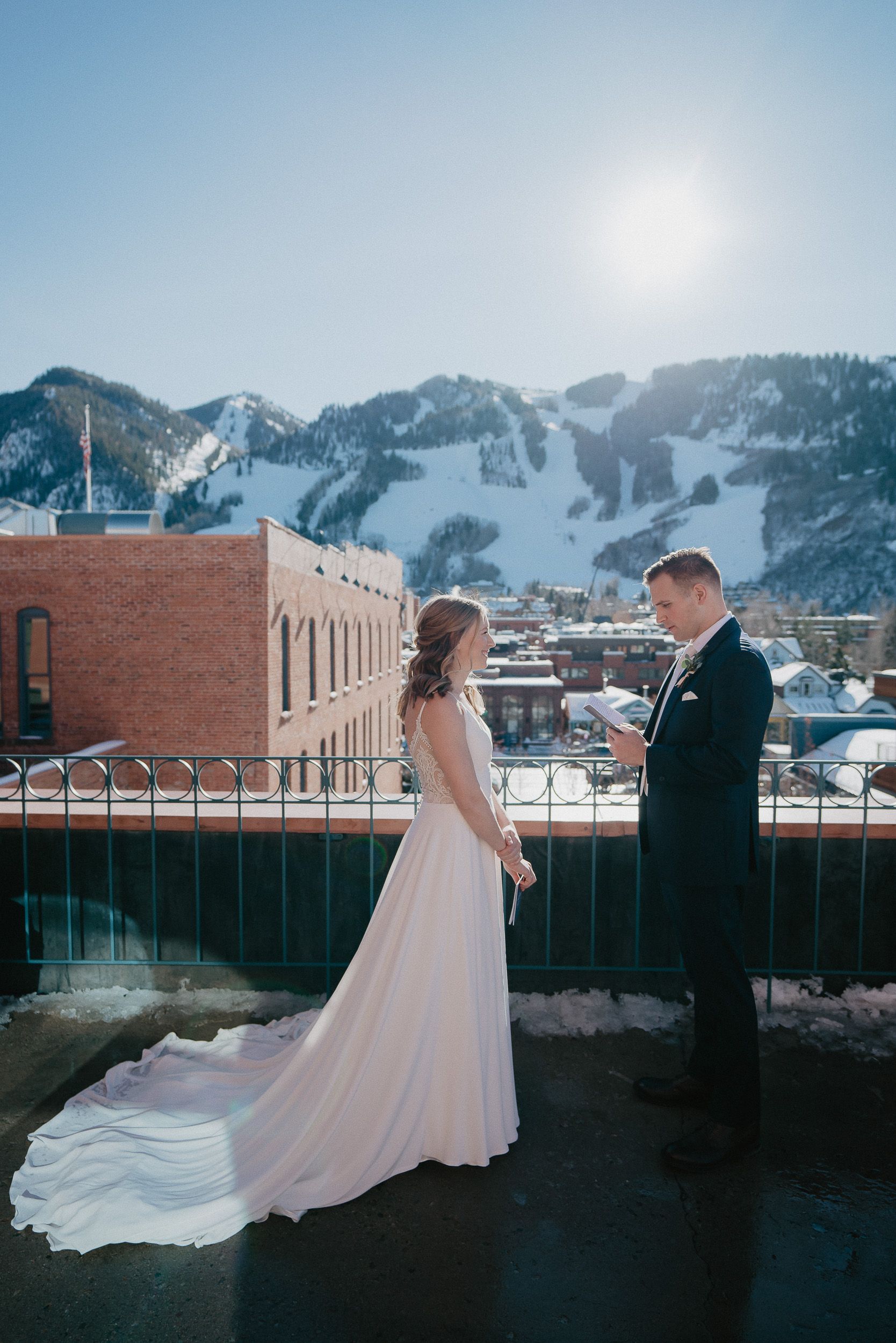 Winter wedding couple on rooftop with snowy mountain ski slopes in background.