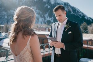 Wedding couple sharing intimate moment on balcony with snow-capped mountains behind them.