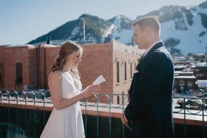 Couple exchanging wedding vows on a rooftop with snow-capped mountains in the background.