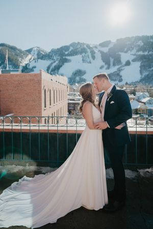 Newlyweds share intimate moment on rooftop with stunning mountain landscape.