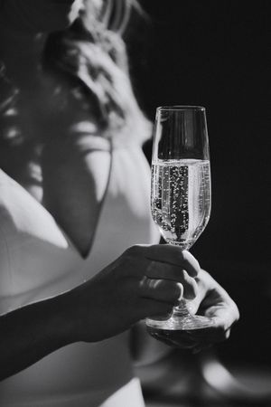 Black and white close-up of champagne flute being held in formal attire.