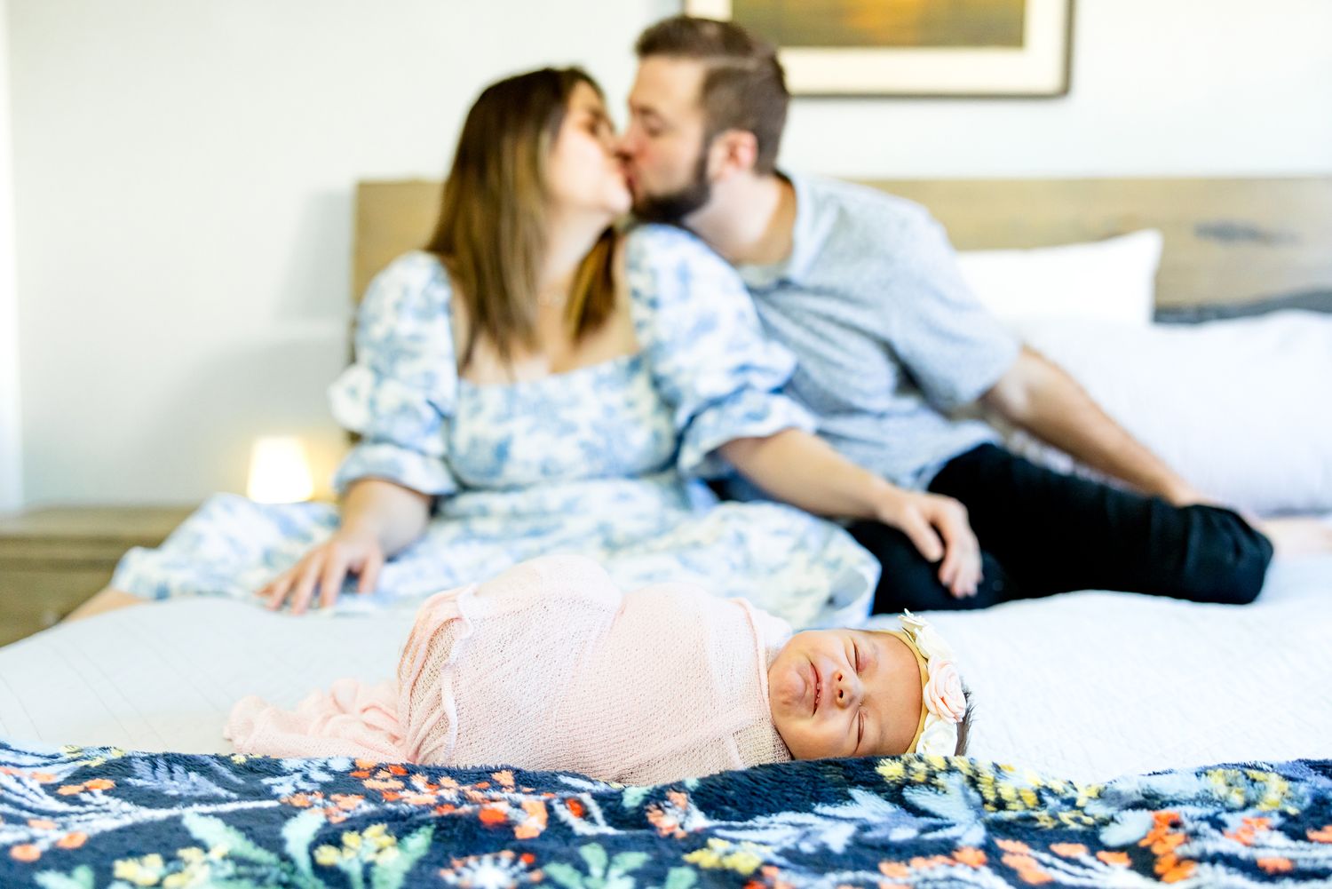 Parents sit and kiss in the background while baby girl sleeps in front of them during newborn photos in Colorado Springs