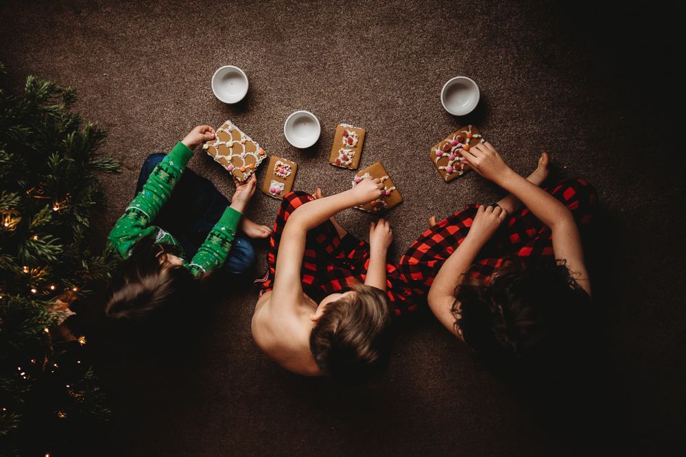 birds eye view of 3 children inspecting ginger bread house pieces beside a xmas tree