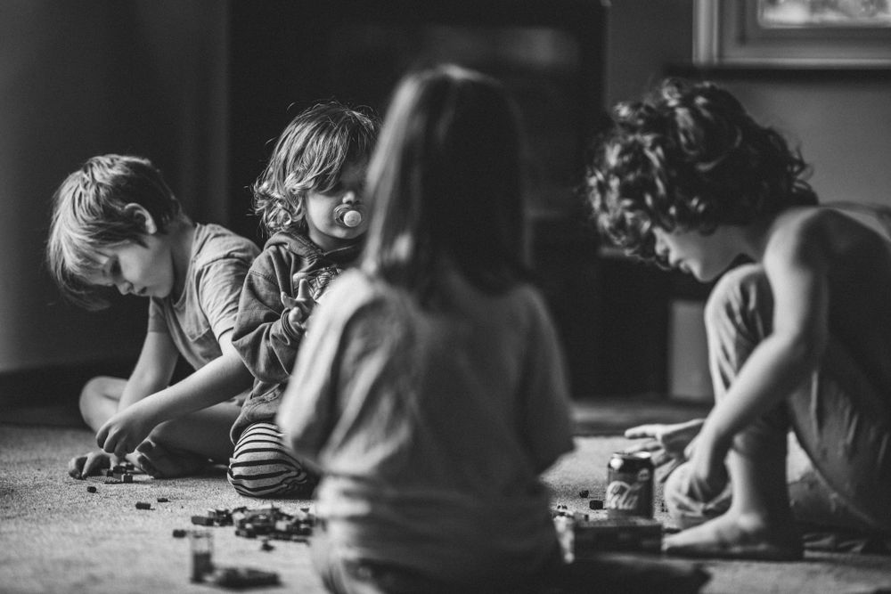 4 children playing games on the floor, a little one in the middle looks on sucking his dummy