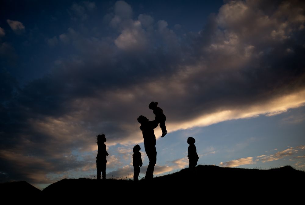 silhouette of 4 children and a man, he is tossing up one of the children above his head