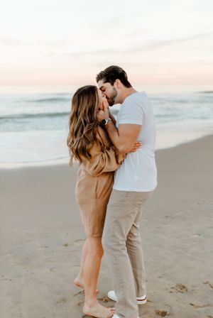 Intimate moment between couple on sandy beach at sunset.