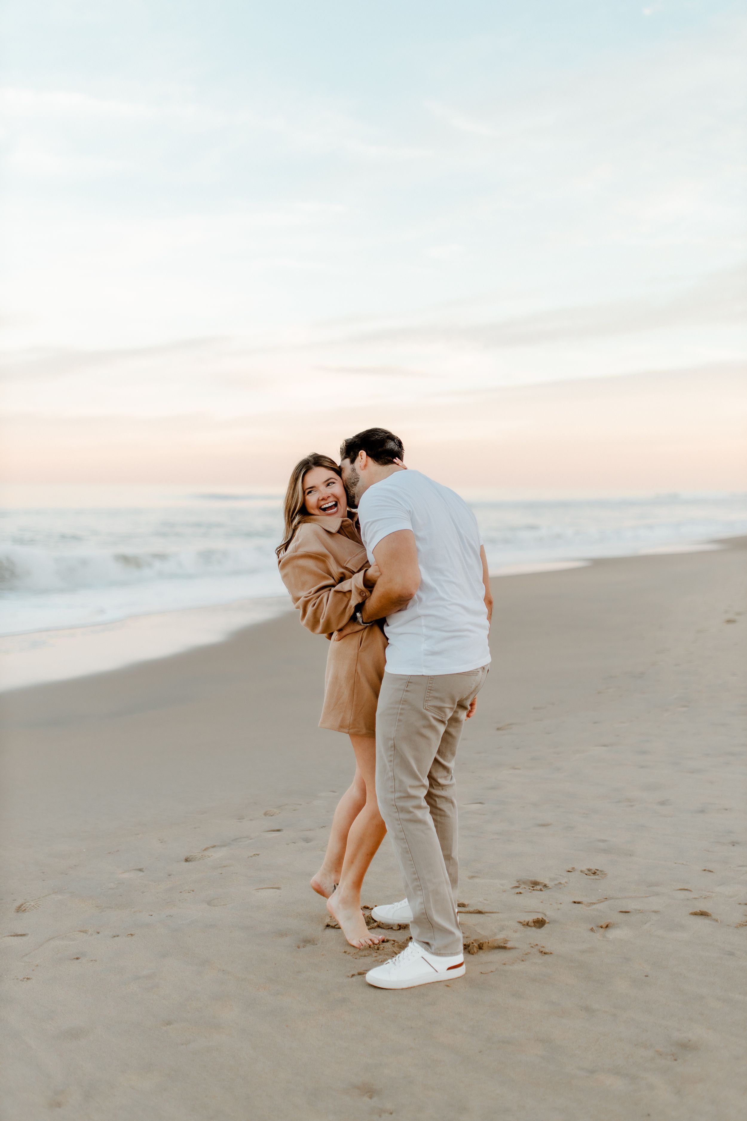 Joyful couple embracing and laughing together on beach at dusk.
