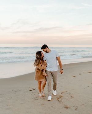 Couple walking together on sandy beach during golden hour.