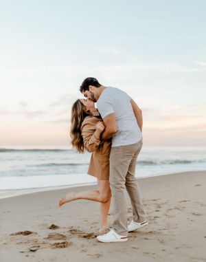 Intimate moment between couple on beach with ocean waves in background.
