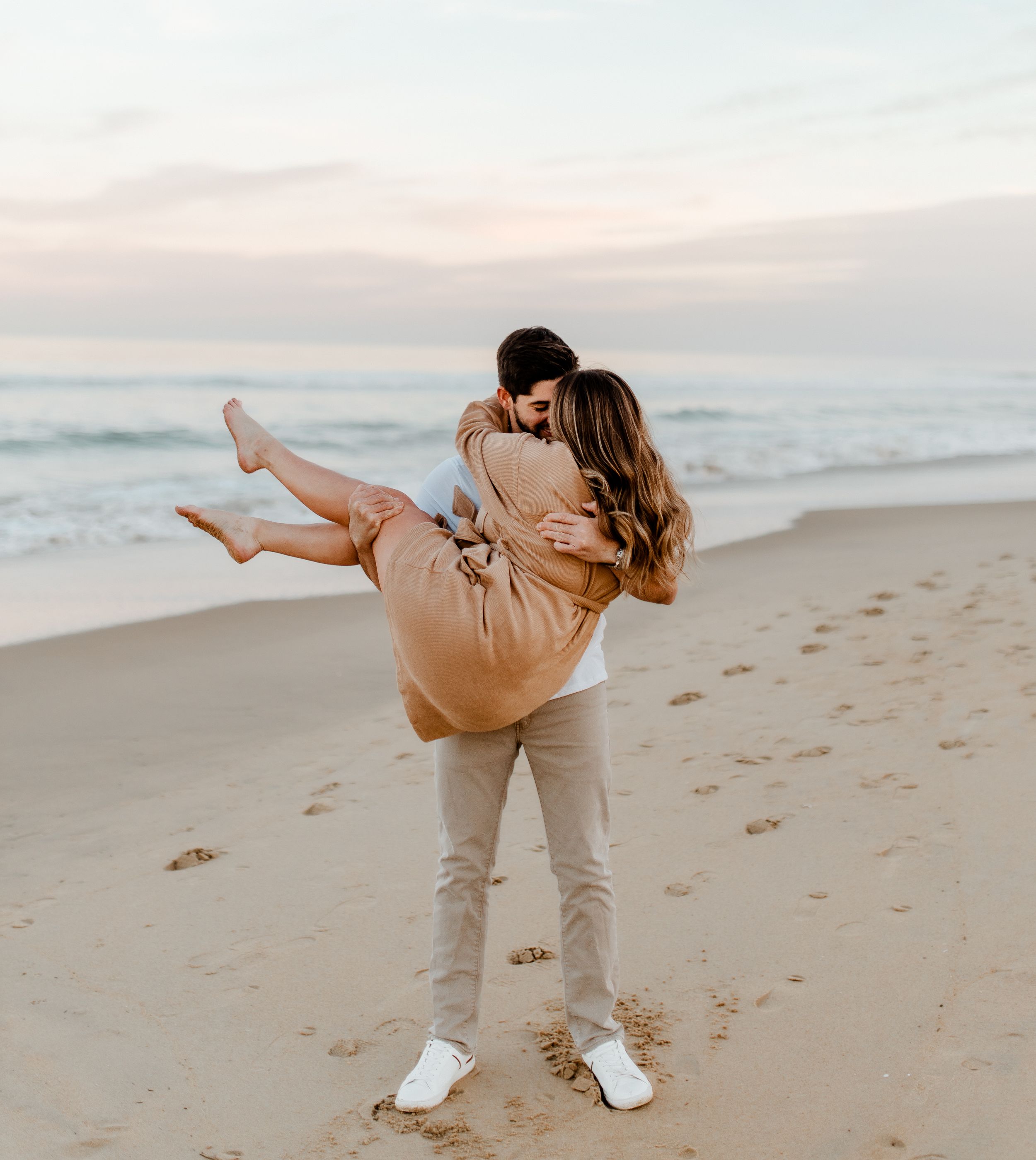 Playful beach photoshoot with couple in casual attire at sunset.