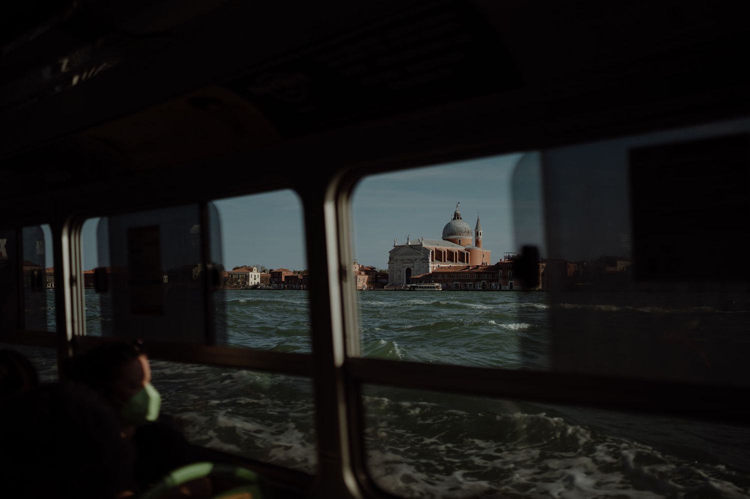 View of a distant building across choppy waters seen through a ferry window frame.