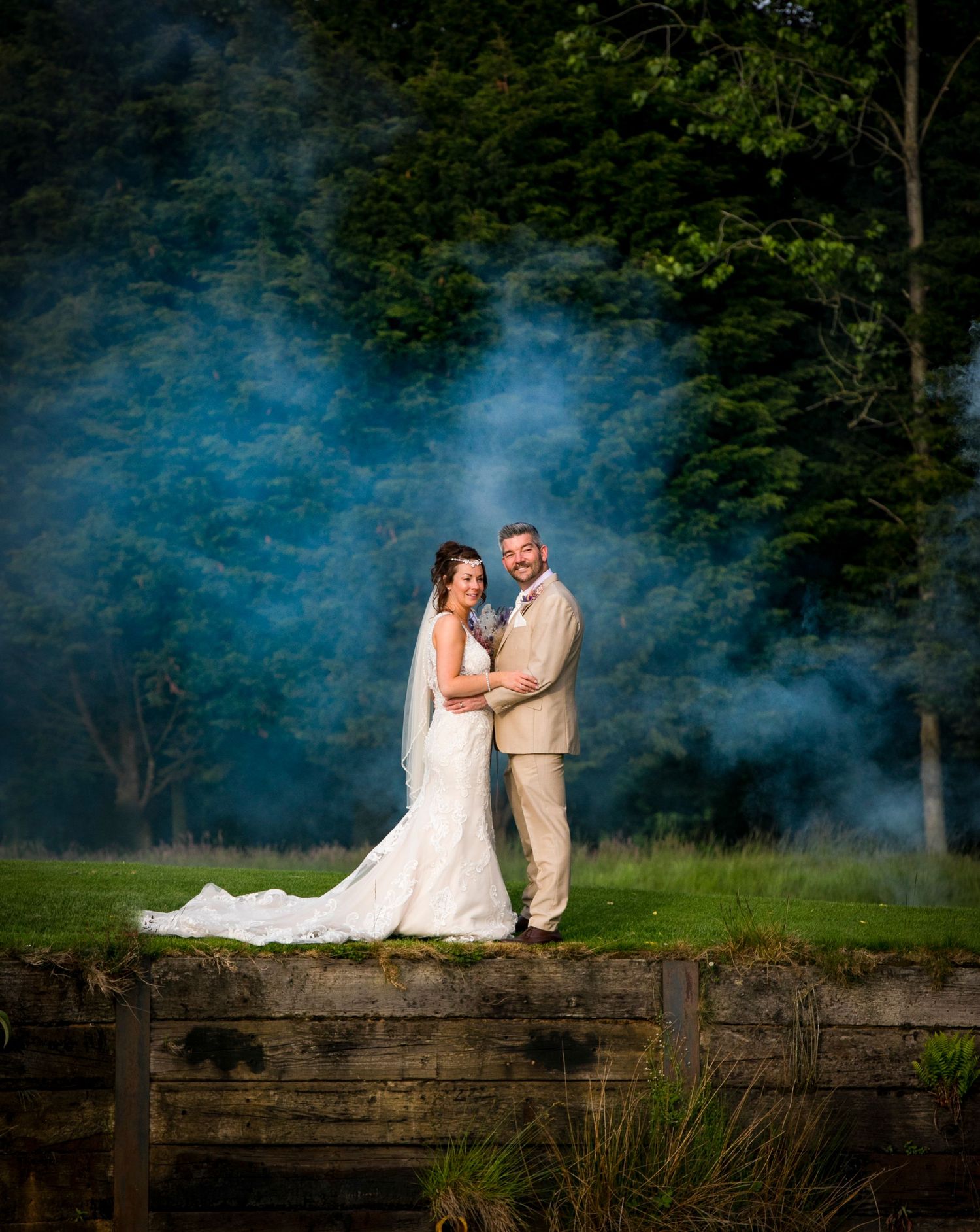 Artistic wedding portraits with blue smoke effects against a rustic wooden fence background.