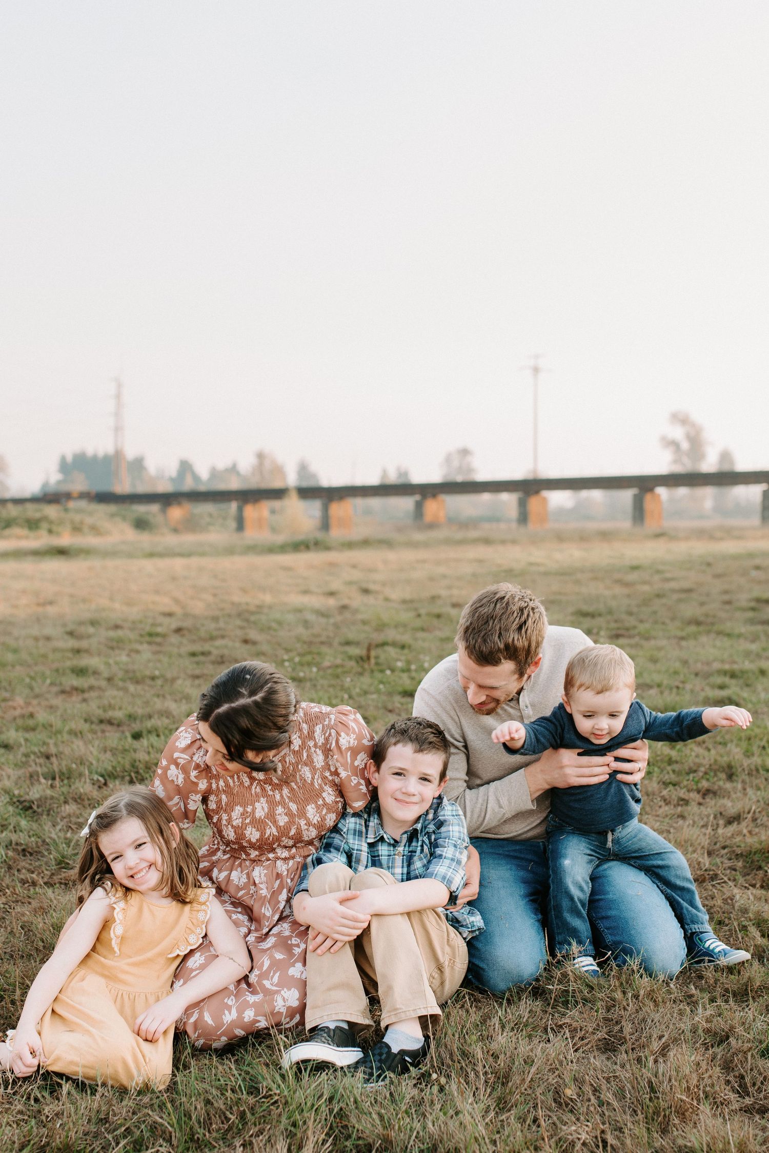 Family lying together in a row on grassy field during sunset photoshoot.