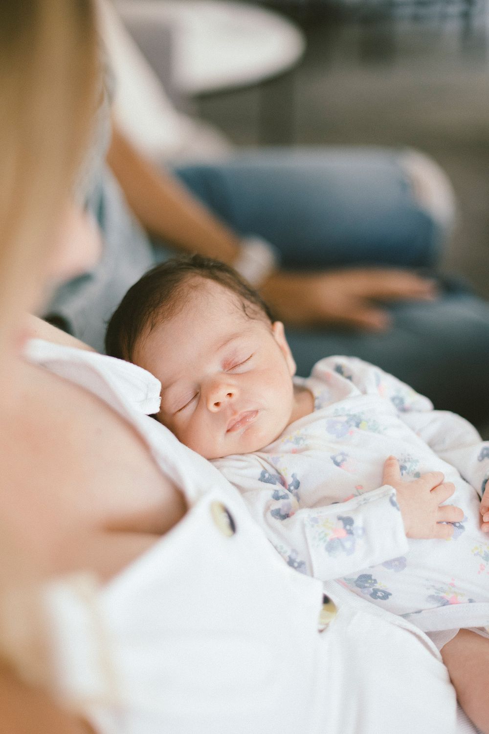 Peaceful sleeping newborn baby in floral onesie resting against parent.