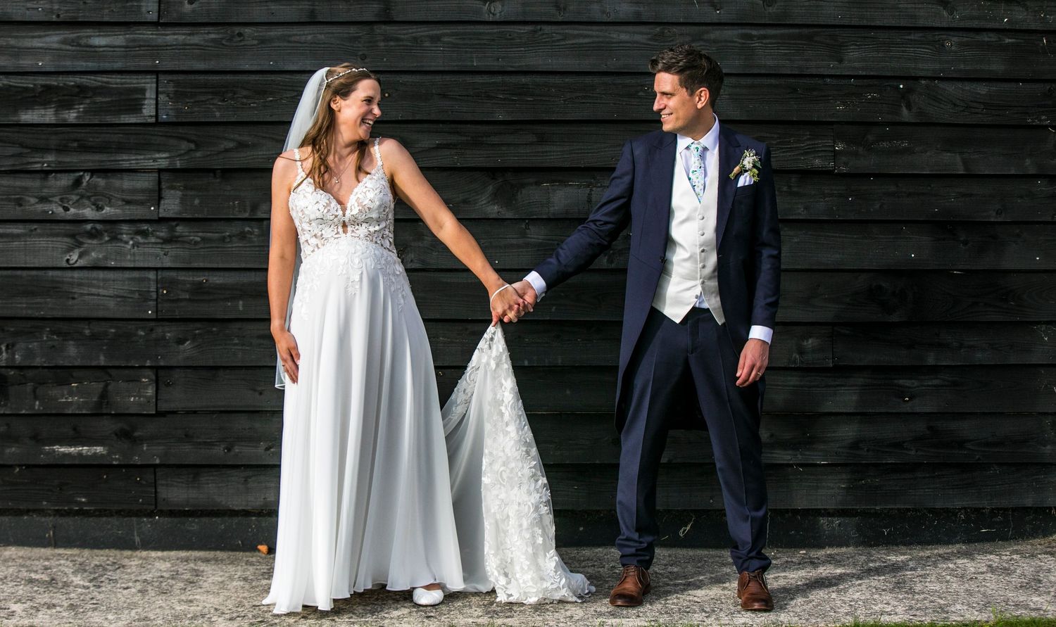 Wedding party posing against dark wooden wall backdrop outdoors.