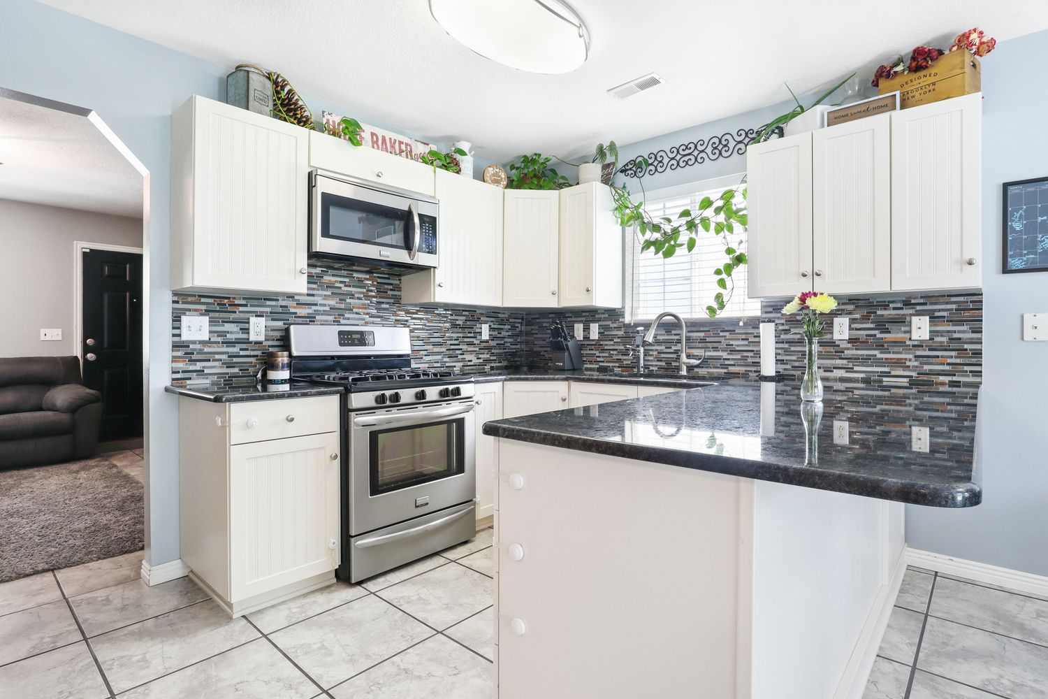 Modern kitchen with white cabinets, dark granite countertops, stainless steel appliances, and tile backsplash.