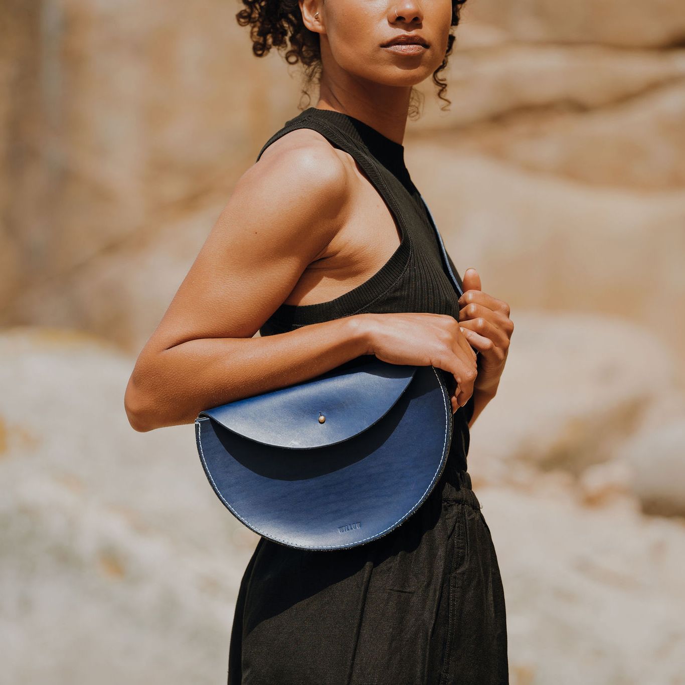 Minimalist fashion photo featuring blue leather handbag against warm desert tones.