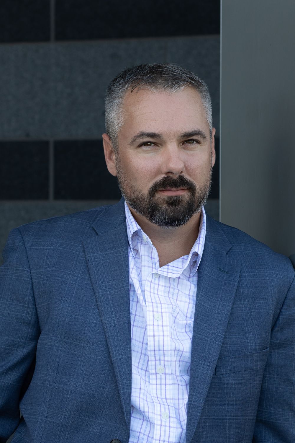 Business portrait of executive in blue plaid blazer and white shirt against dark background.