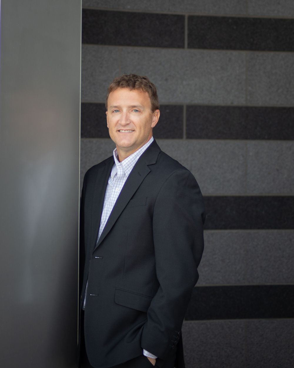Professional portrait in dark suit against modern striped wall background.