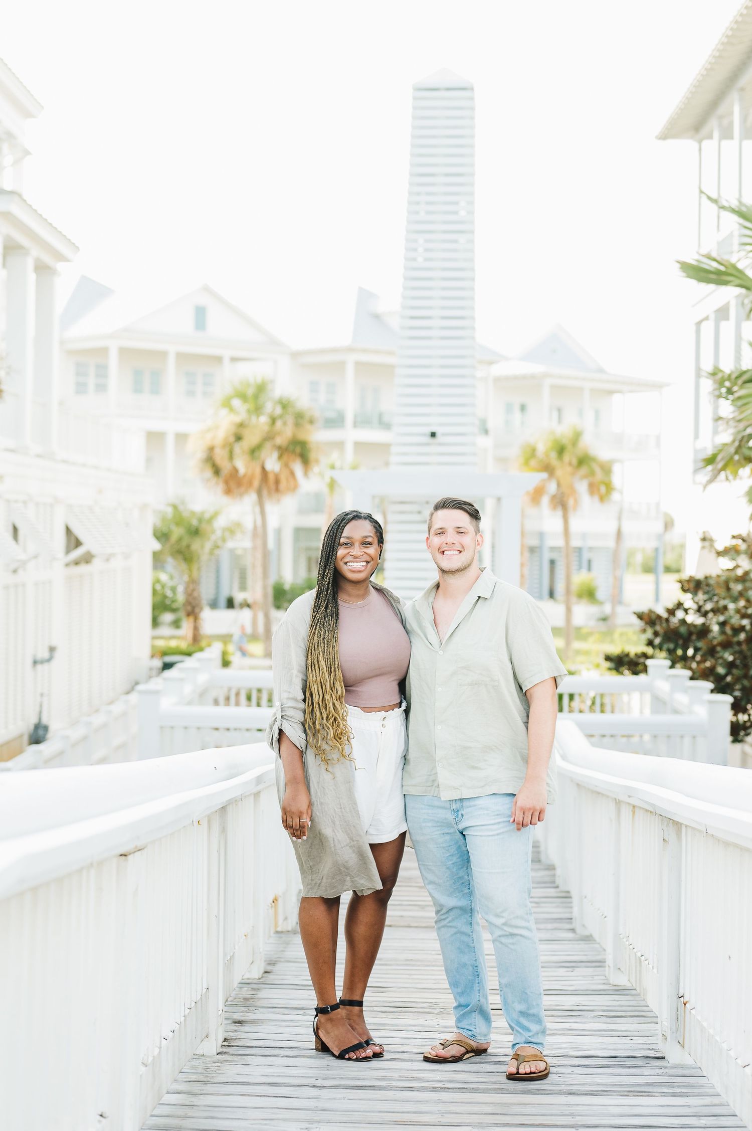 Couple walking hand in hand on elevated white wooden walkway near beach.