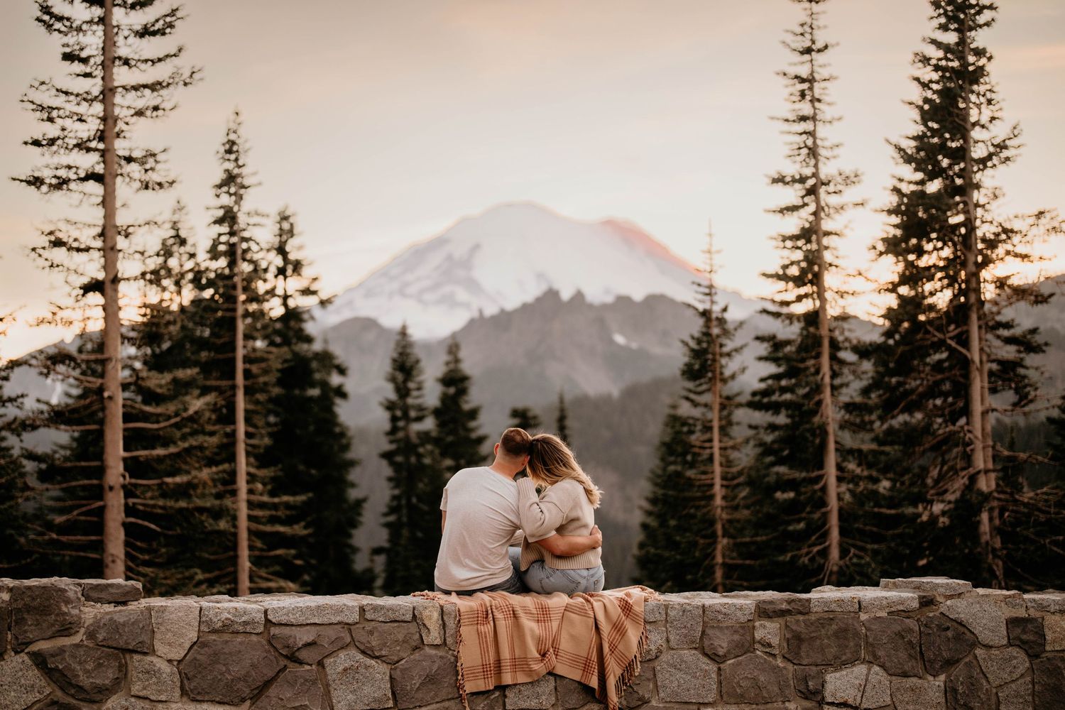 Couple sitting on rock wall at Lake Tipsoo holding eachother for engagement photos