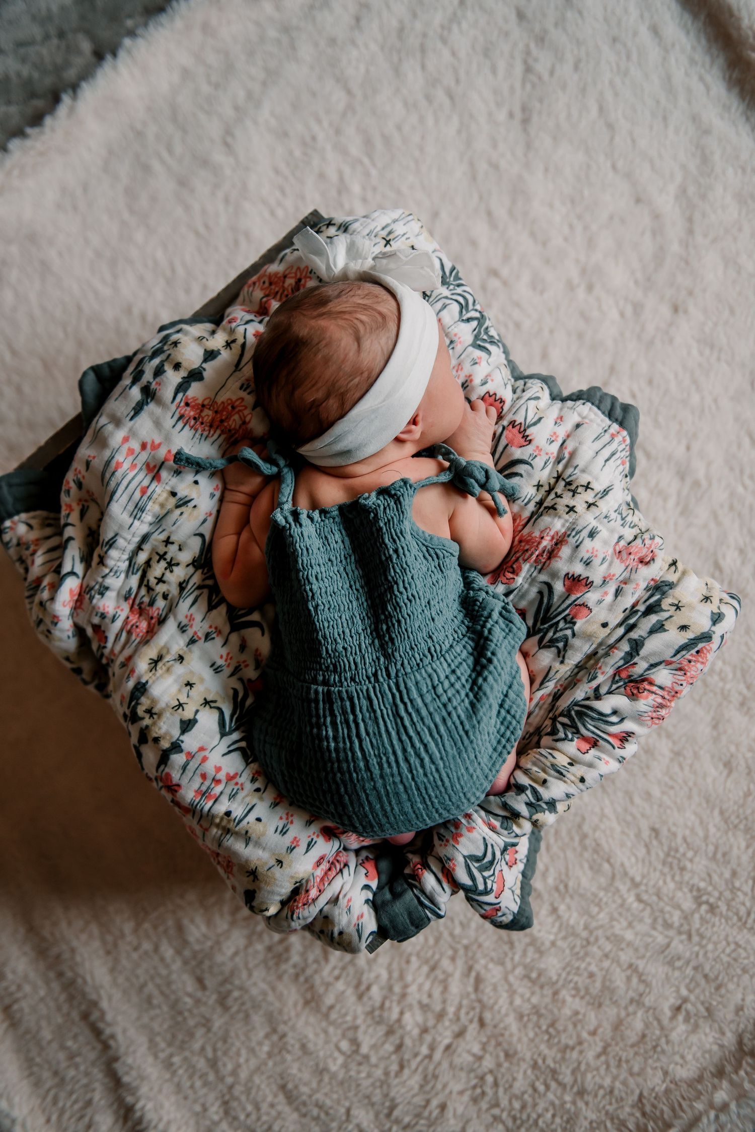 Newborn baby wearing teal knit outfit sleeps on floral blanket.