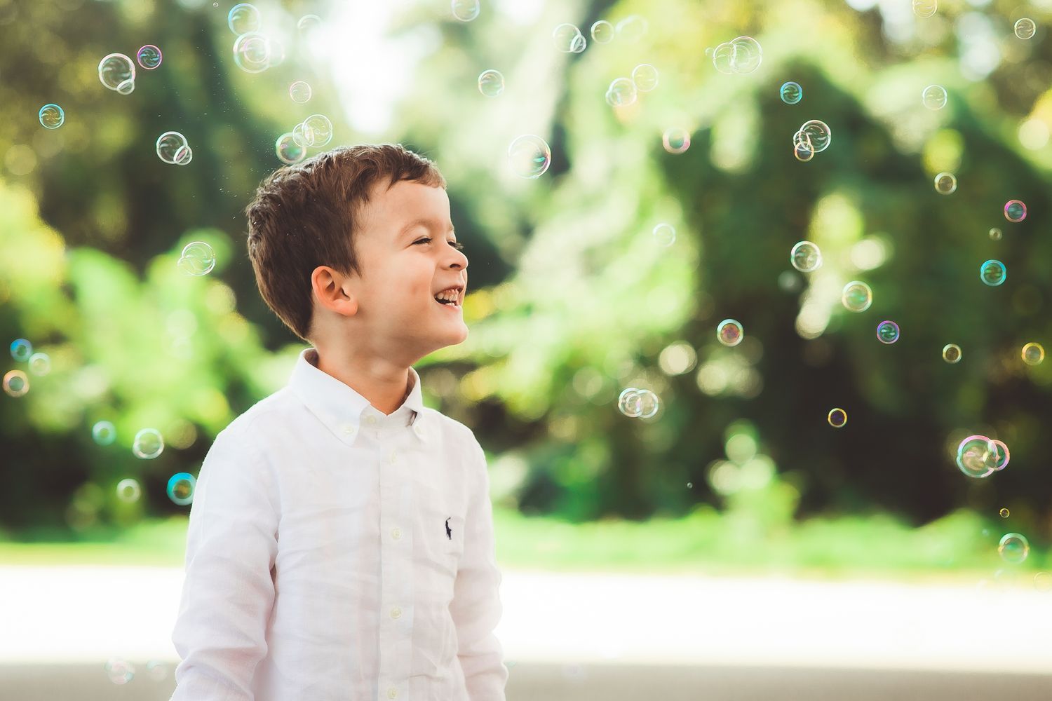 Child laughing with pure joy as soap bubbles float in sunny outdoor setting.