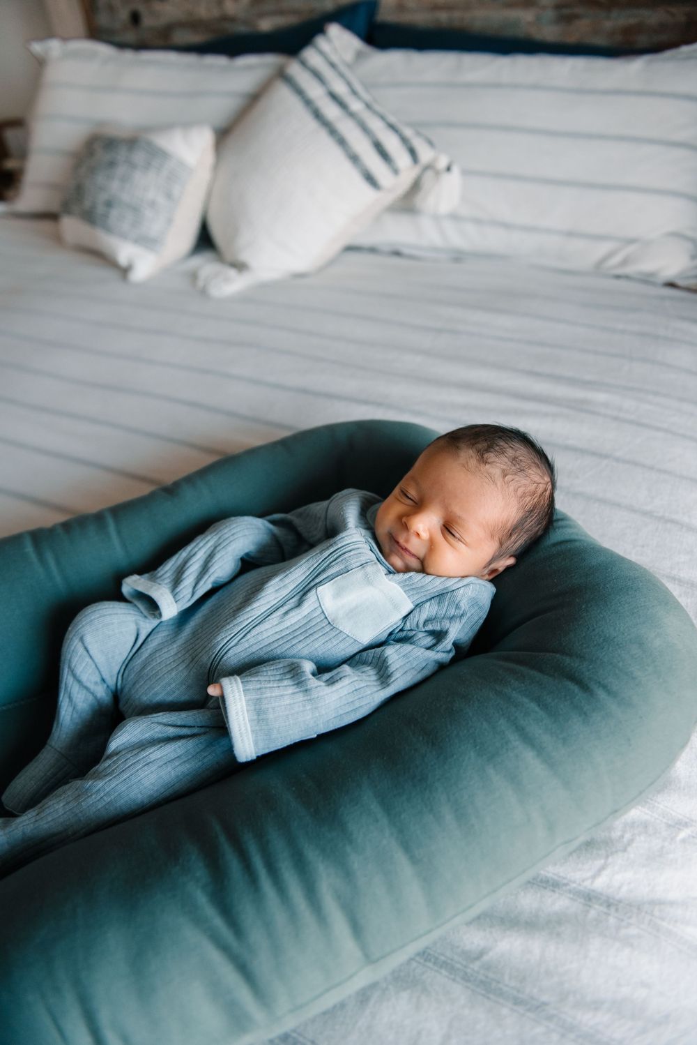 Baby resting peacefully on teal pregnancy pillow surrounded by white bedding.