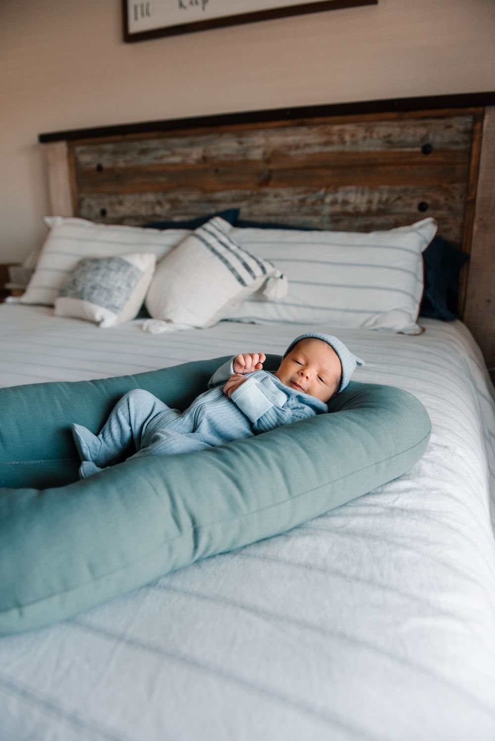 Baby sleeping peacefully on teal pregnancy pillow against white bedding.