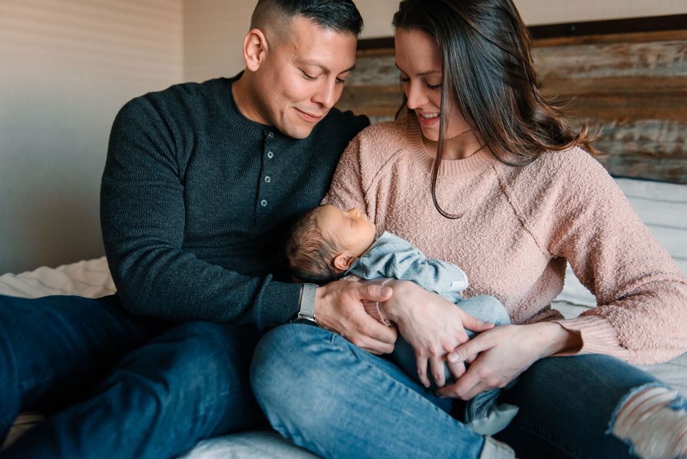 Parents sharing tender moments with their sleeping newborn on a cozy bed.