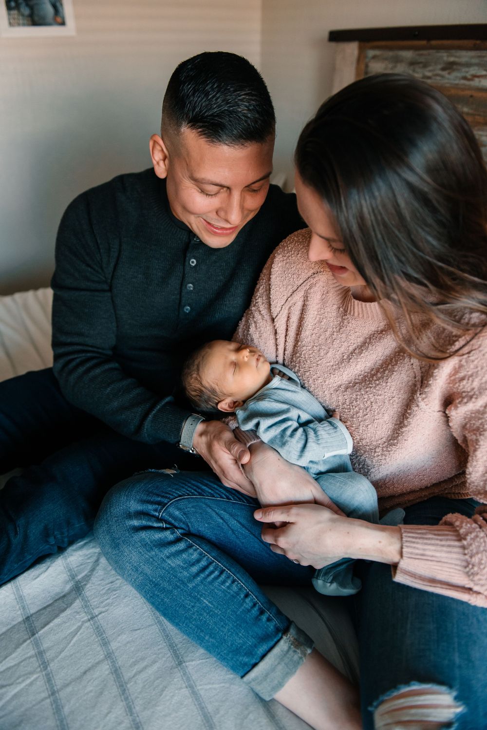 Intimate family moment showing parents cradling a newborn baby on a bed.