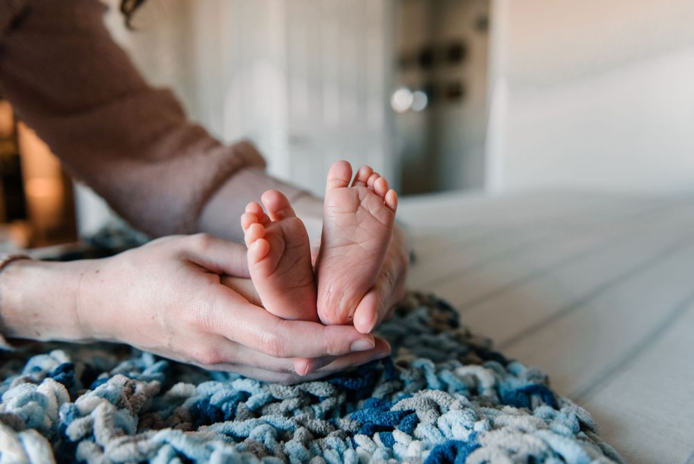 Close-up of tiny baby feet resting on a blue knitted blanket.