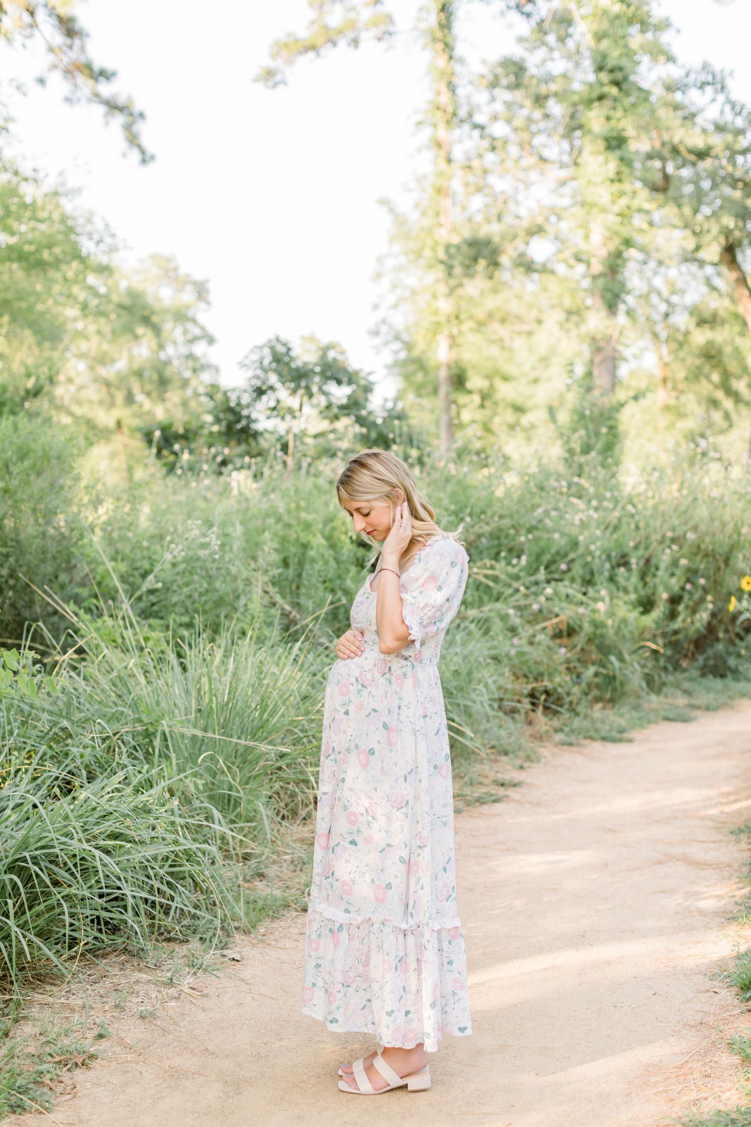Ethereal maternity photo on dirt path surrounded by lush greenery.