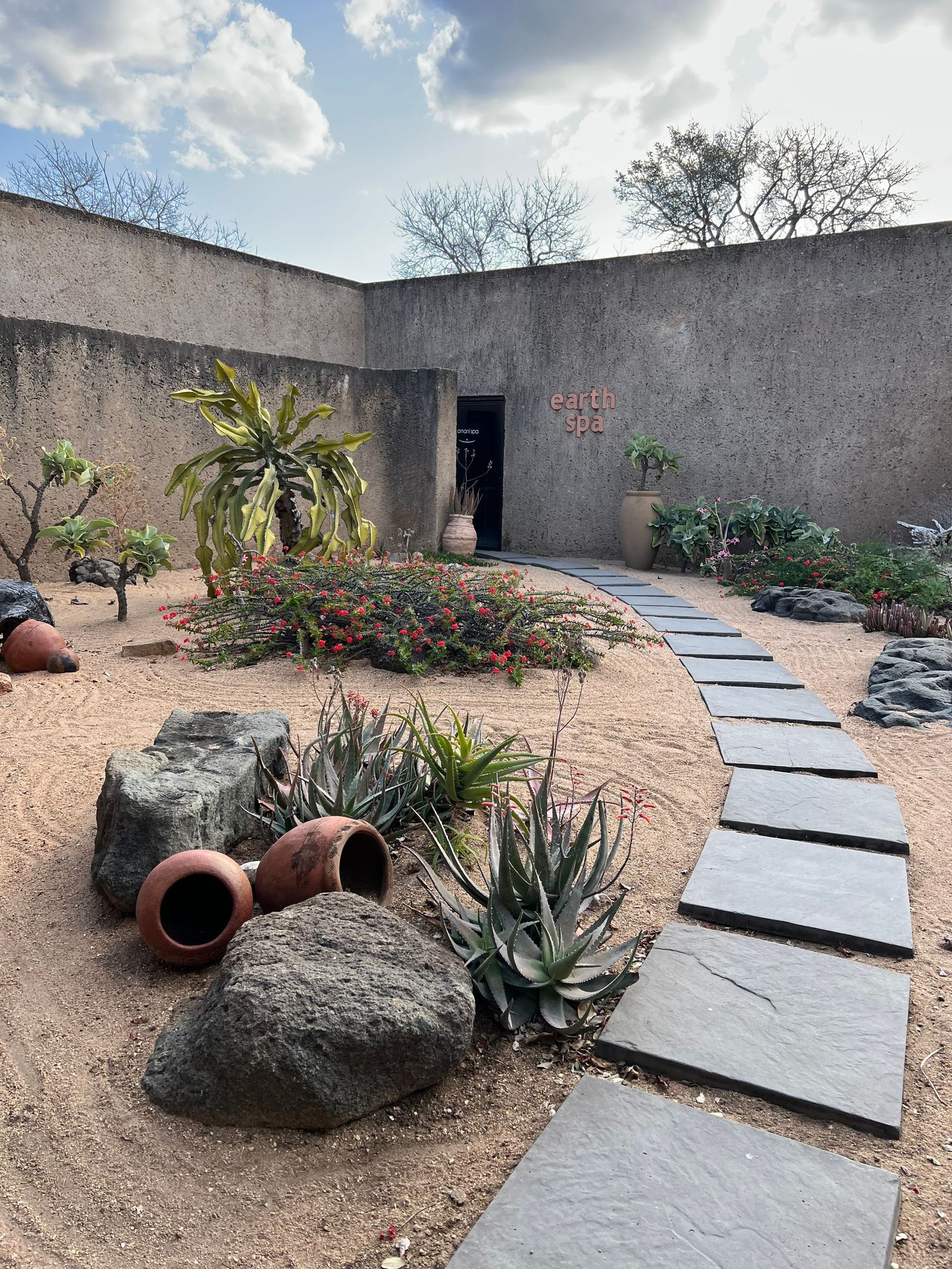 Desert garden pathway with stone slabs leading through succulents and decorative boulders to a doorway.
