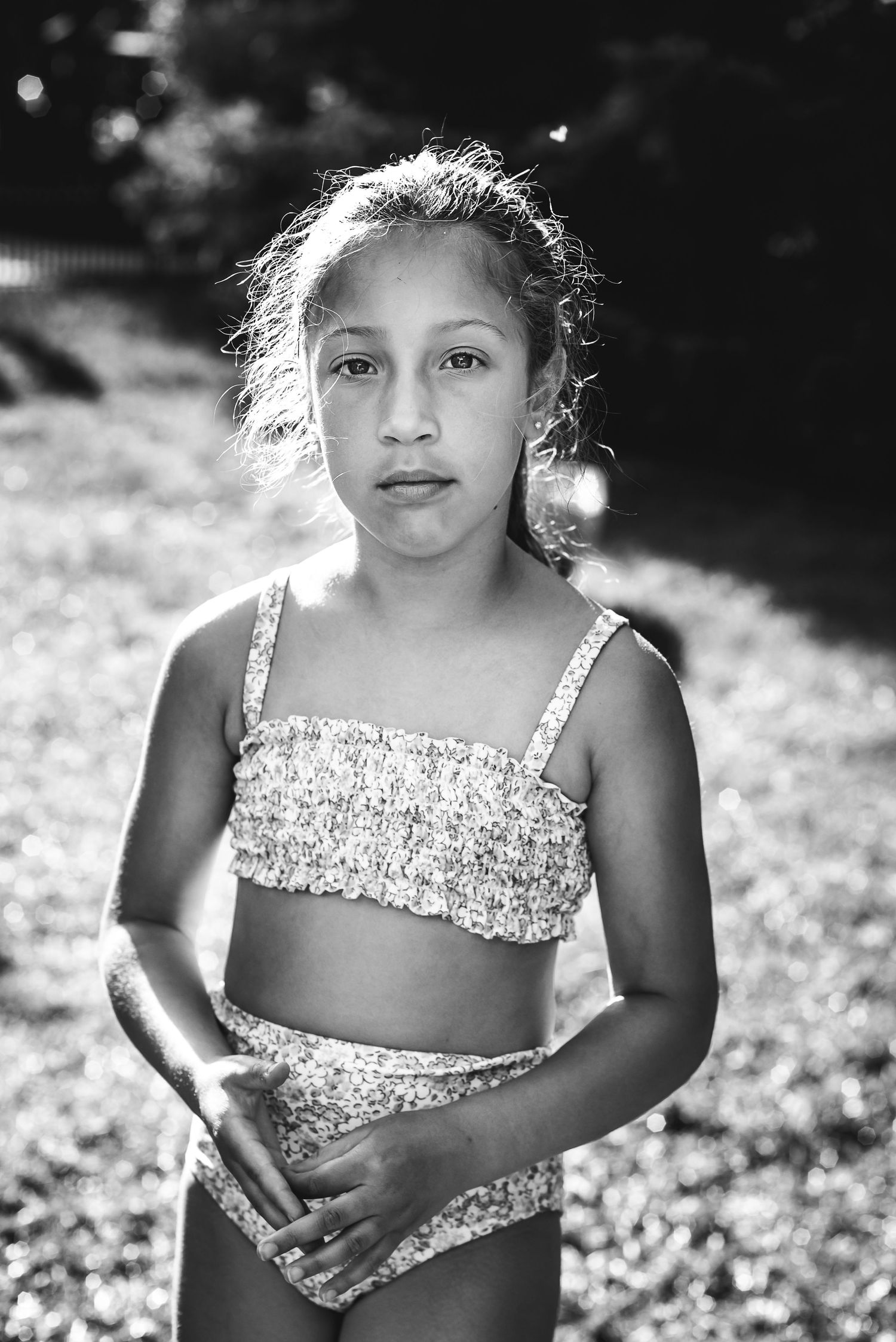 BW image of a girl standing on the grass, backlit by the sun.