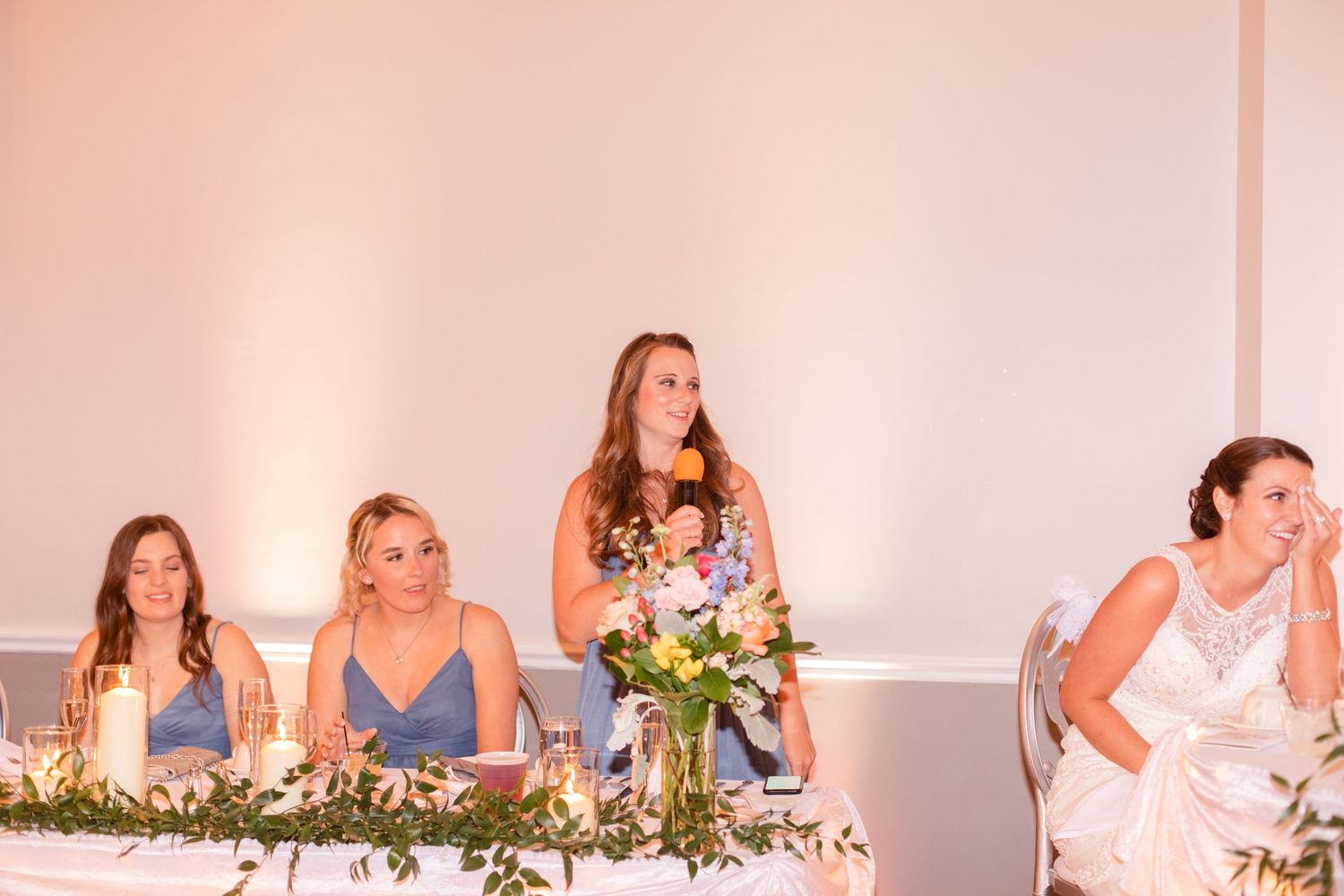 Wedding reception guests enjoying dinner at tables adorned with pink and white floral centerpieces.