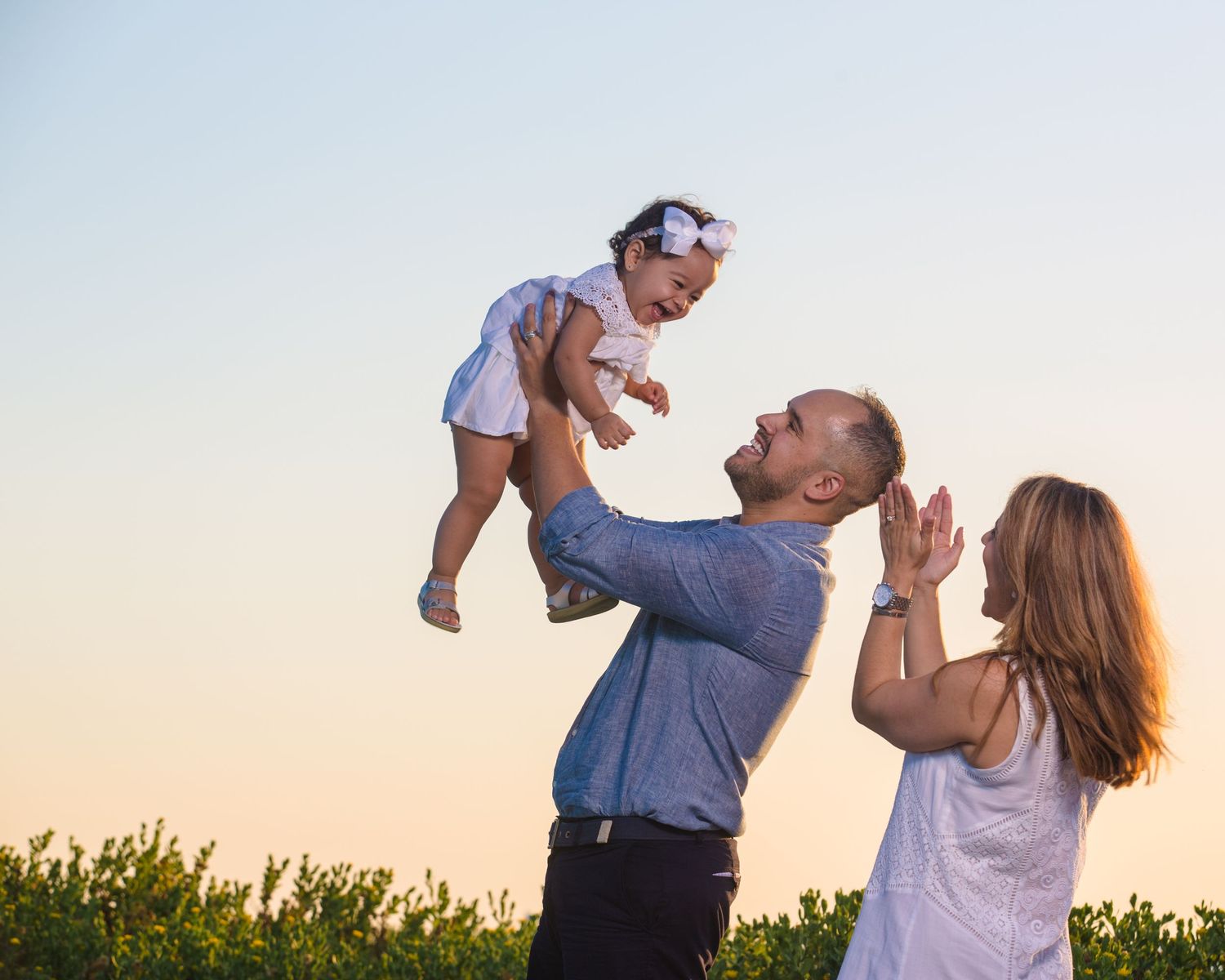 A playful family photoshoot sequence at sunset in a grassy field.