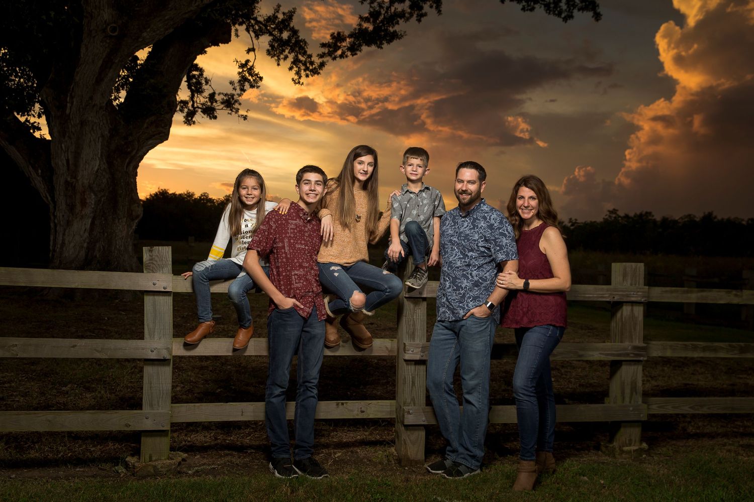 Group of friends posing on wooden fence during sunset.