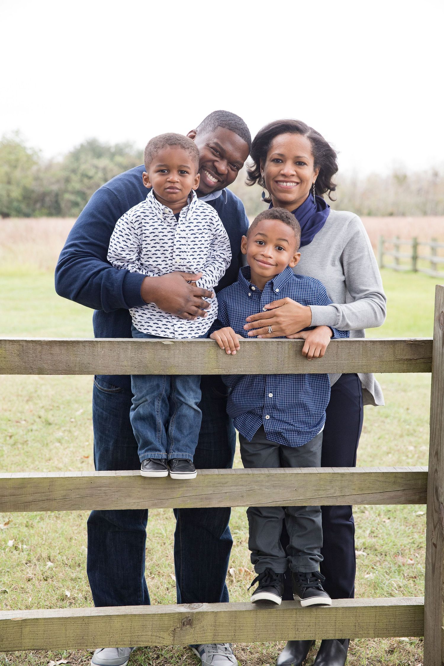 A family leaning on a wooden fence during an outdoor photo session.