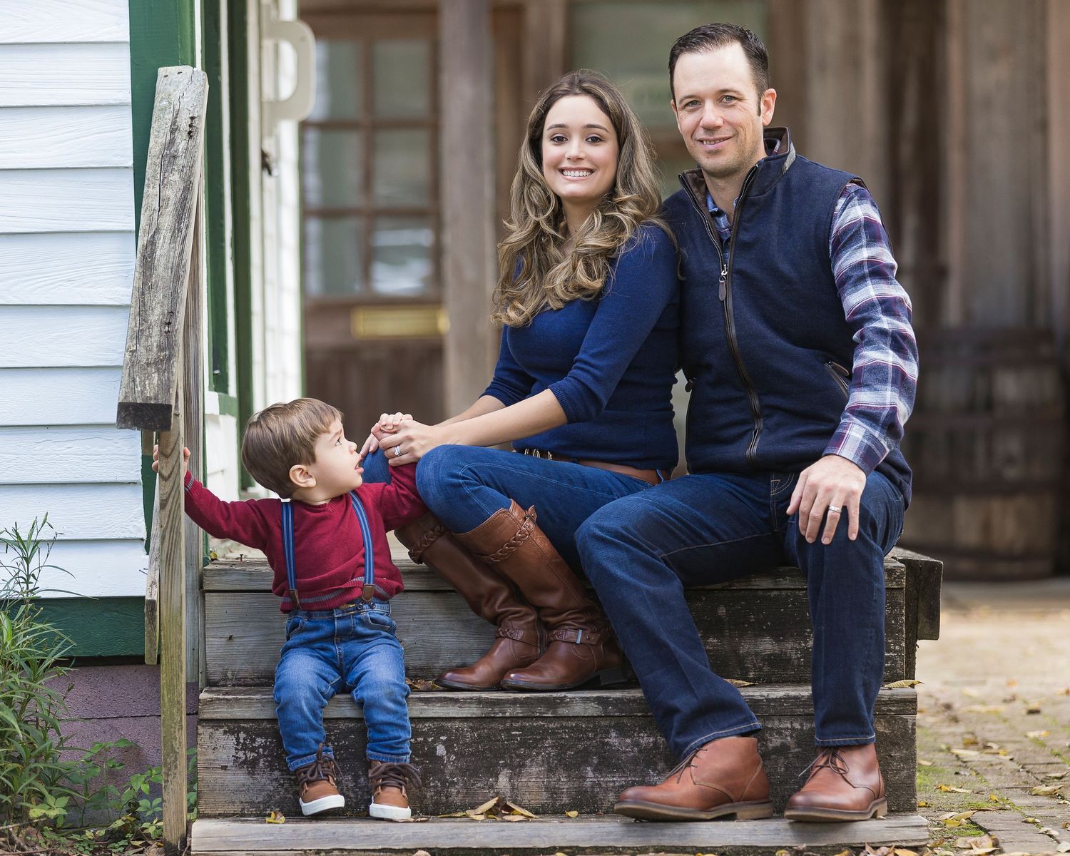 Family sitting on front porch steps of white house.