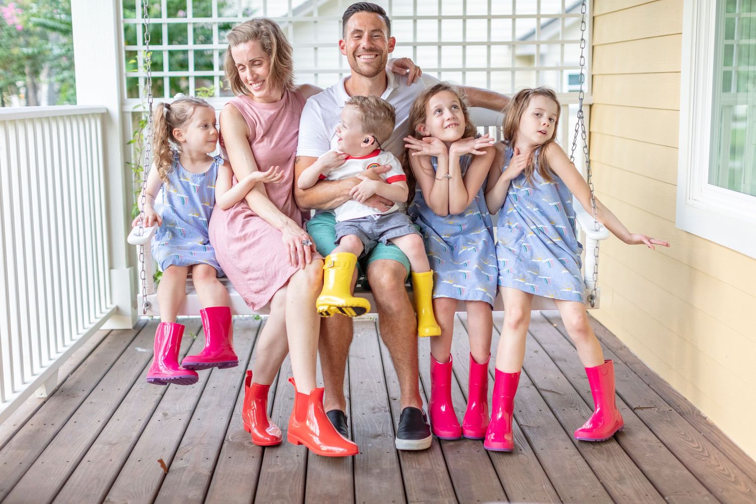 Group wearing colorful rain boots sitting together on wooden porch steps.
