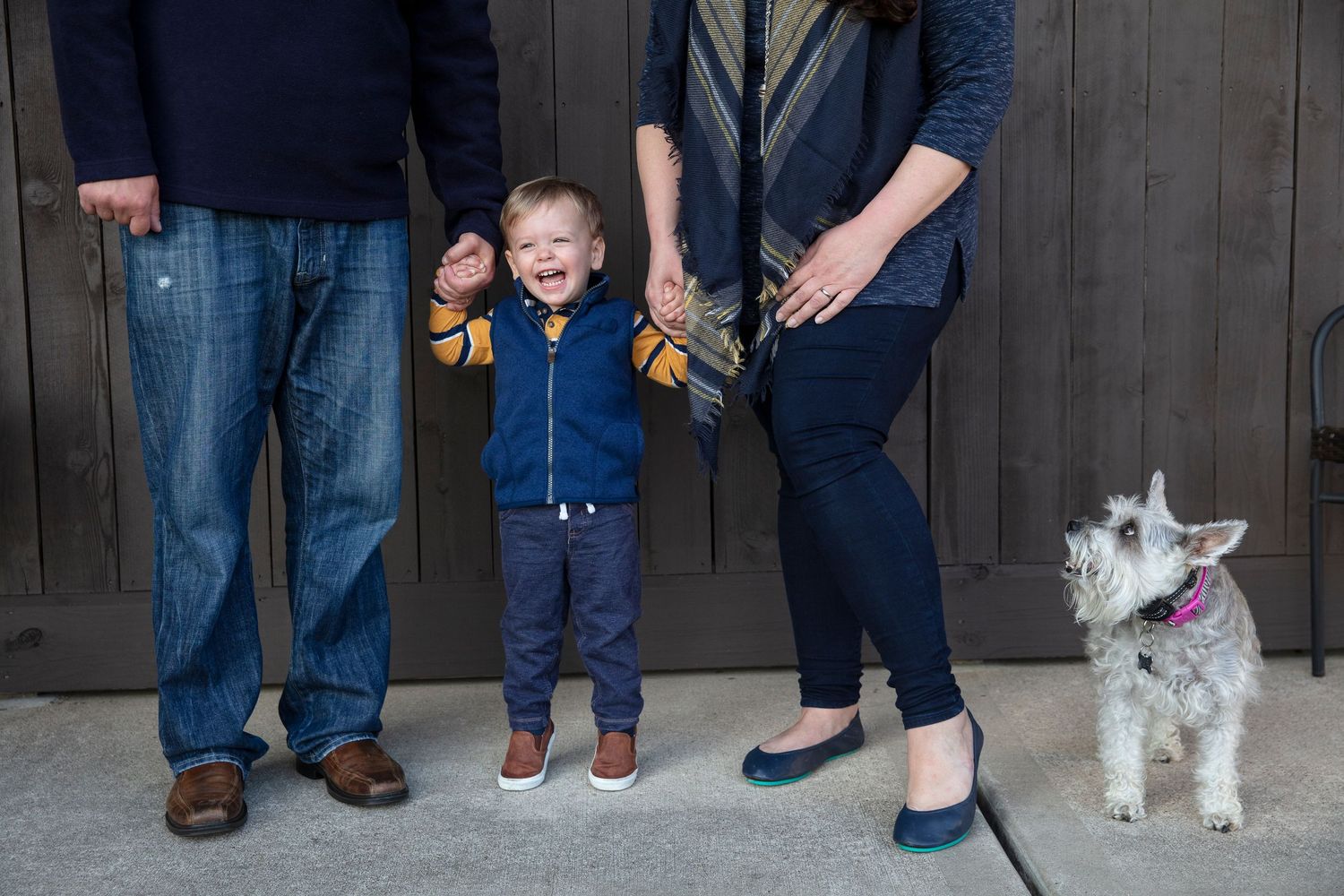 White terrier dog posing with family members in casual attire against dark fence.