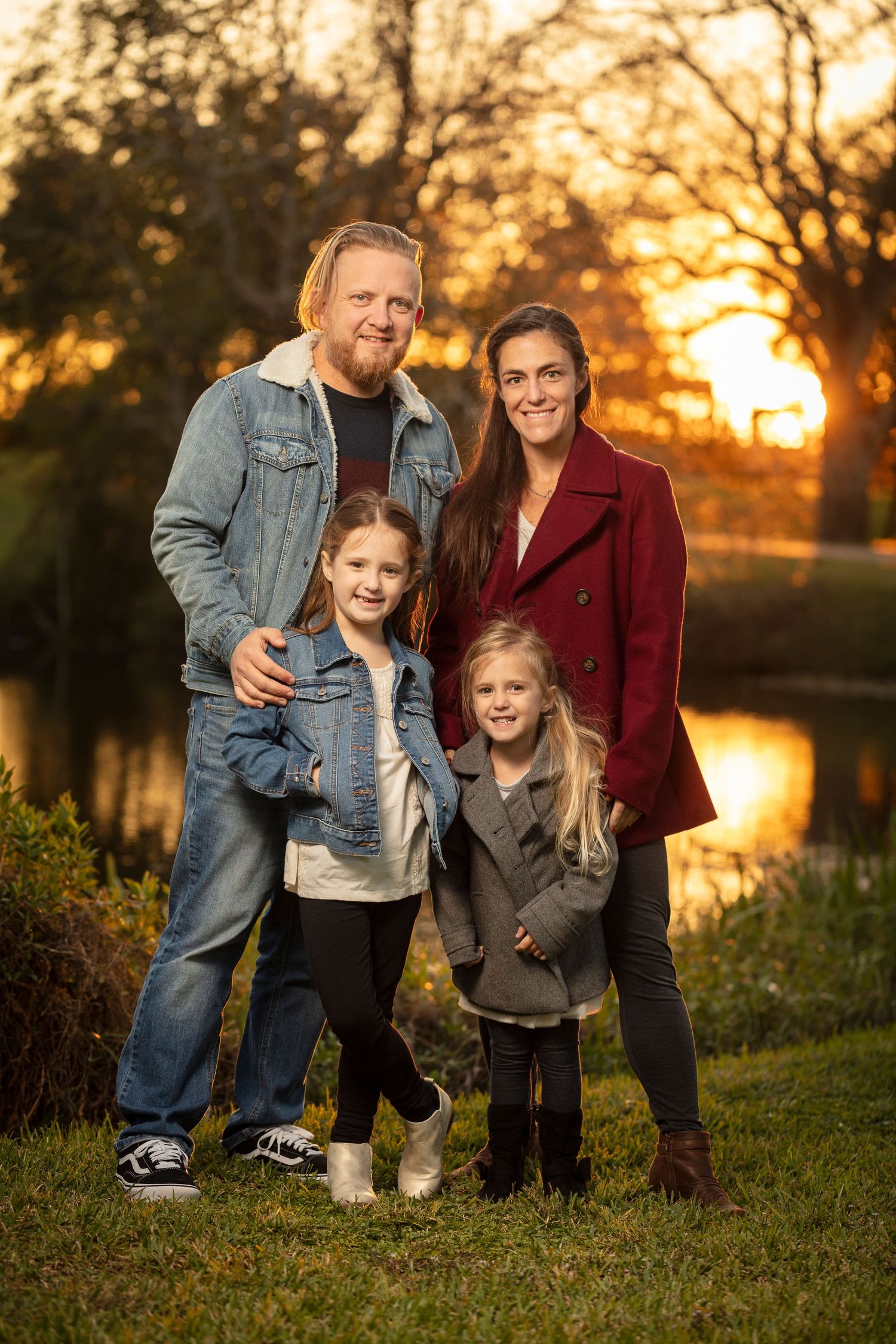 Family of four poses by pond during golden sunset in park.