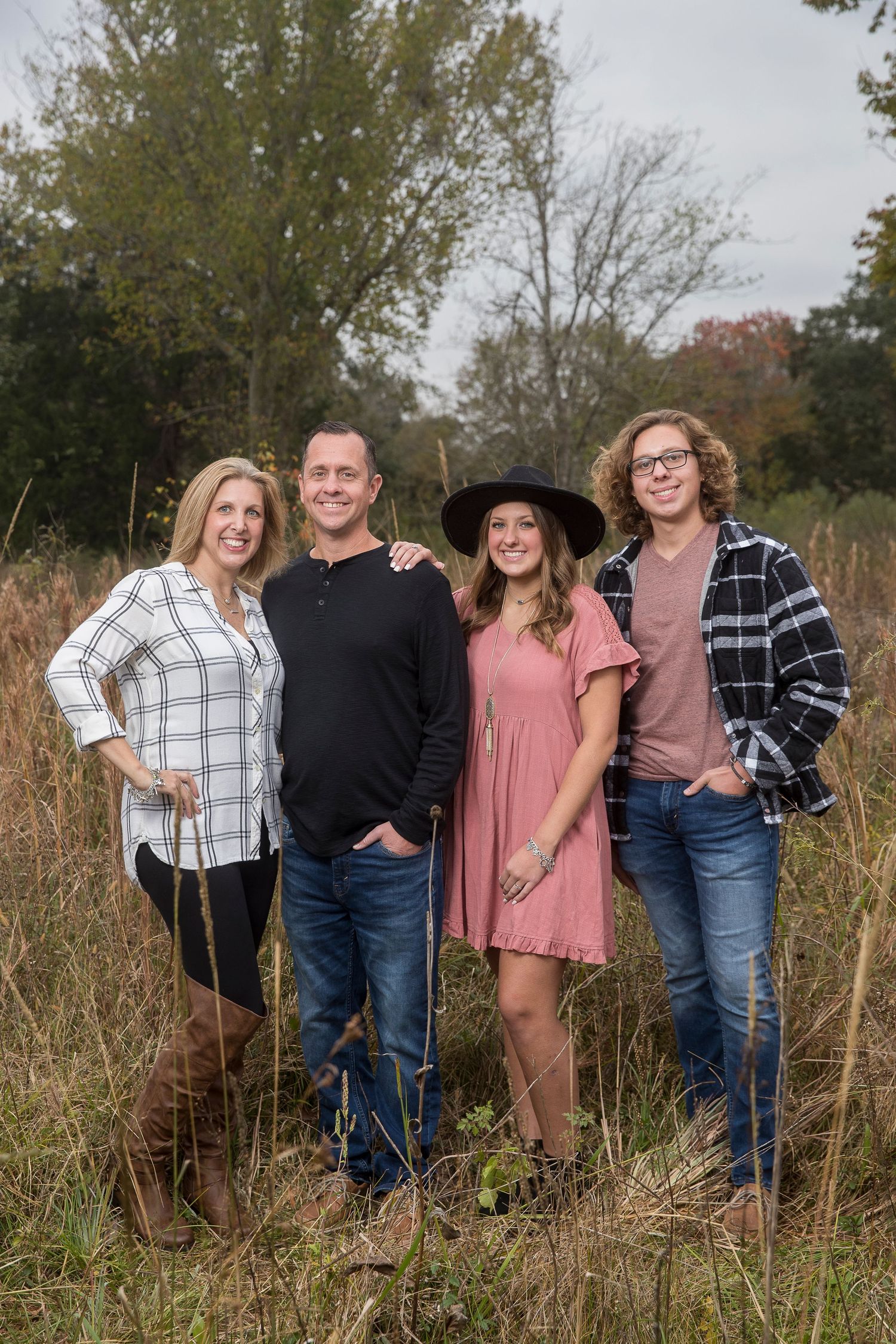Group portrait of family members in casual attire standing in tall autumn grass.