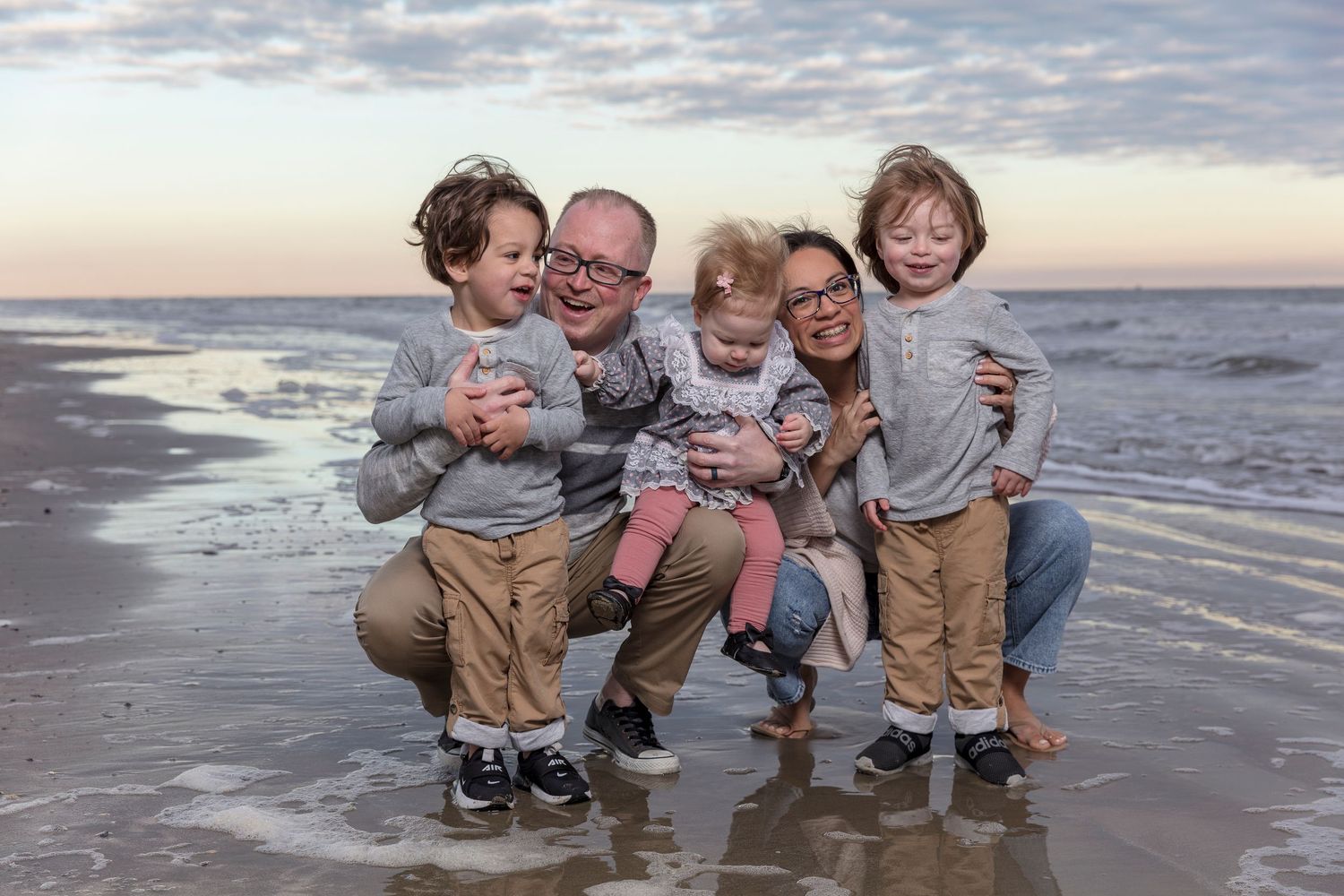 Family plays together at beach during sunset with waves in background.