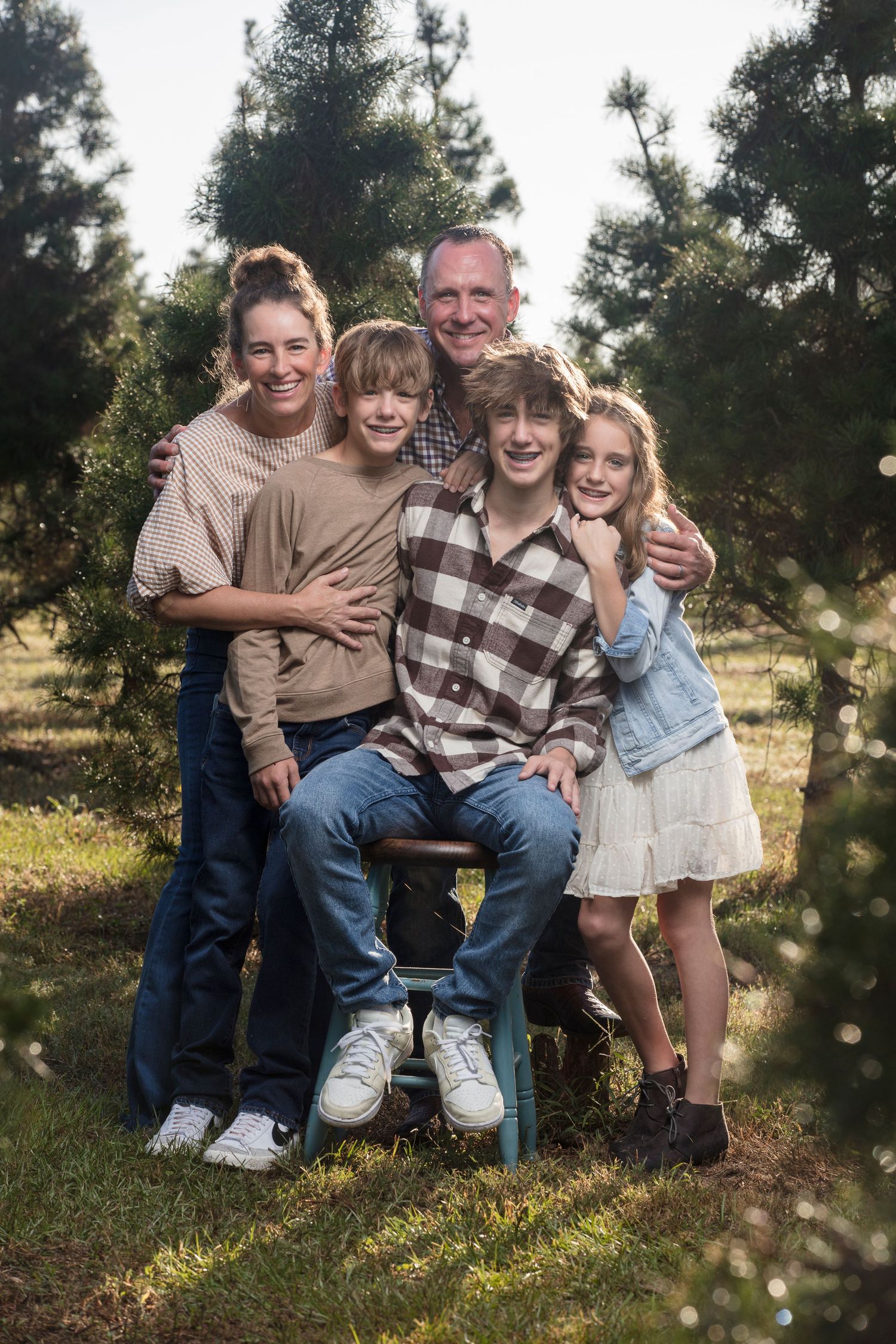 Casual family photo session with everyone sitting together outdoors among pine trees.