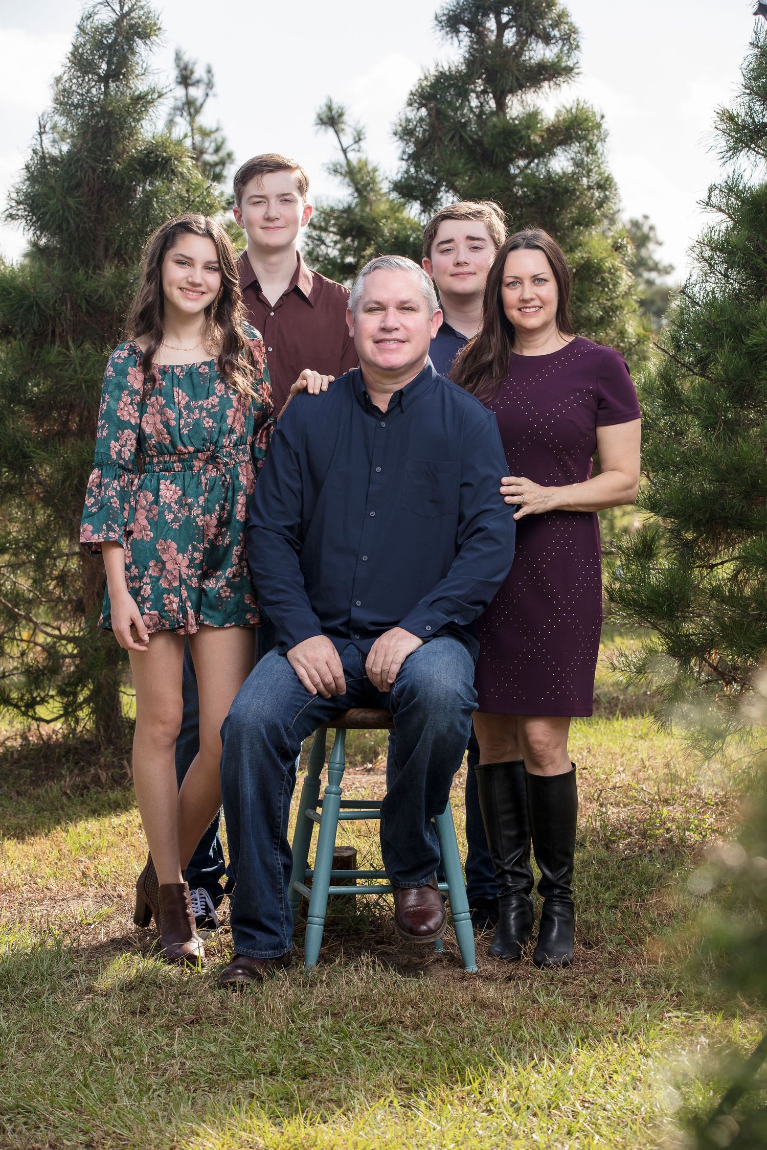 Family group portrait outdoors with pine trees in the background.