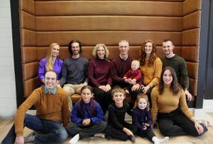 Large family group photo with adults and children posed together in front of wooden wall panels.