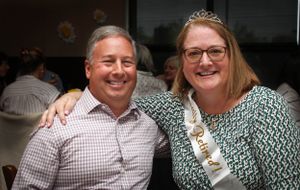A festive celebration moment captured with two people posing together, one wearing a tiara and sash.