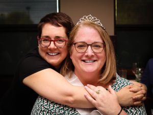 Two people embracing and smiling while wearing party attire with a tiara.